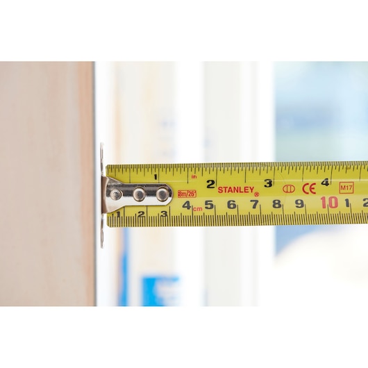 STANLEY 5-33-891 yellow tape measure in use measuring a wooden surface, close-up side view.