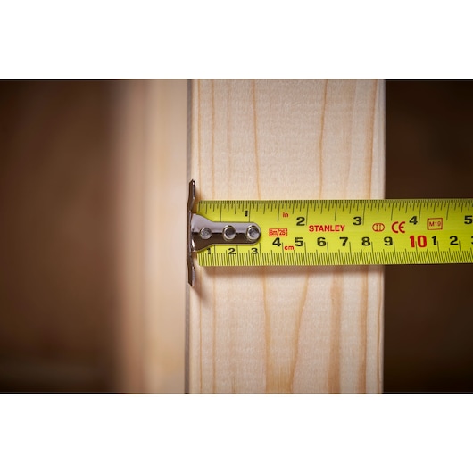 STANLEY 5-33-891 tape measure measuring wooden beam, close-up, clear metric markings.