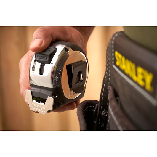 Photo of STANLEY 5-33-891 tape measure in hand next to tool belt with STANLEY logo, close-up view.