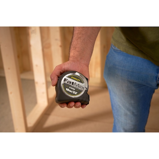 STANLEY 5-33-896 tape measure held in hand, FatMax Xtreme, black and silver, construction setting.