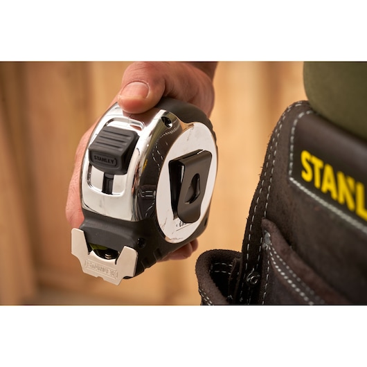 Photo of STANLEY 5-33-896 tape measure held in hand near STANLEY tool belt, close-up shot.