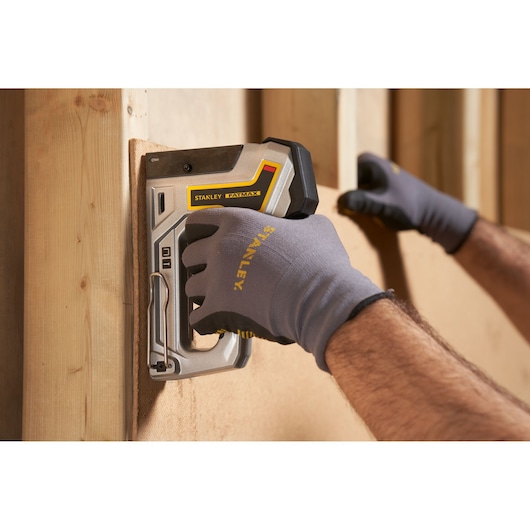 Photo of STANLEY 6-TR350 stapler in use, held by gloved hands attaching panel to wooden frame.