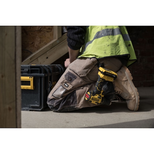 STANLEY FMC627D2 cordless drill in holster, worker kneeling next to STANLEY toolbox, indoor construction setting.