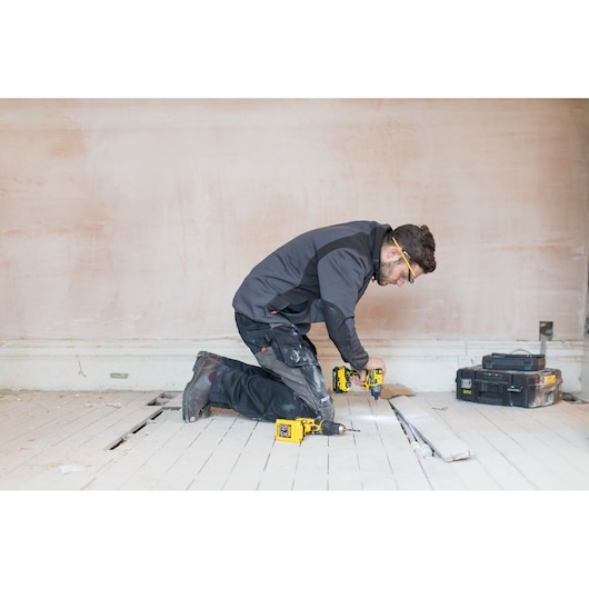 STANLEY FMC647B cordless drill used by worker on floor, with toolbox and pipes nearby, wide room view.