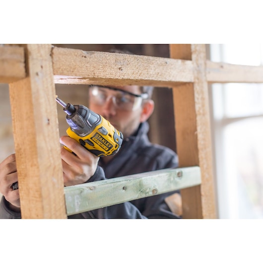 Photo of STANLEY FMC647B cordless screwdriver in use on a wooden frame, close-up showing hand operation.