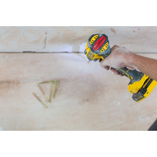 Stanley FMC647B cordless drill held in hand, close-up angle, yellow and black design with dust-covered workspace.