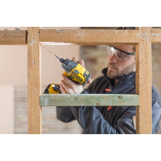 Photo of STANLEY FMC647D2 impact driver used on wood frame by person in dark jacket.