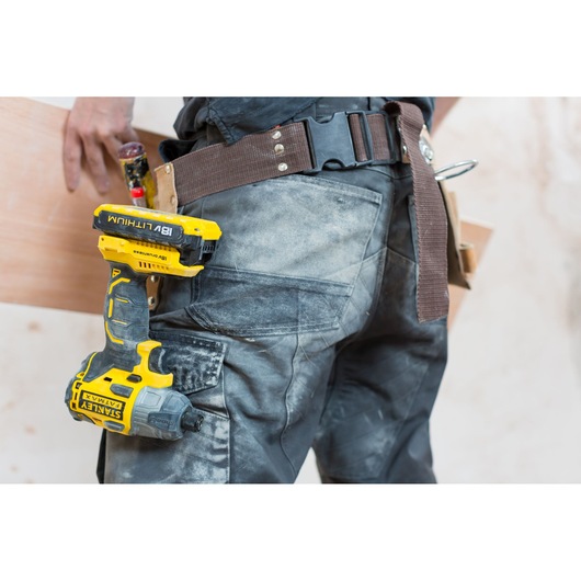 Photo of STANLEY FMC647D2 impact driver on a work belt, worn by a construction worker in dusty pants.
