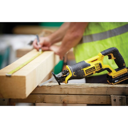 STANLEY FMC675B cordless reciprocating saw on a wooden beam, with person measuring wood in background.
