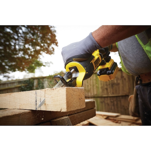 STANLEY FMC675B reciprocating saw cutting wood outdoors, close-up of tool and gloved hand in use.