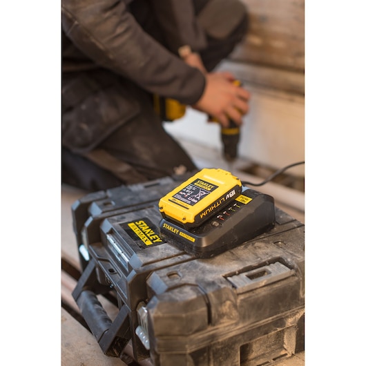 STANLEY FMC687L 18V lithium battery on charger, placed on a rugged toolbox at a worksite.