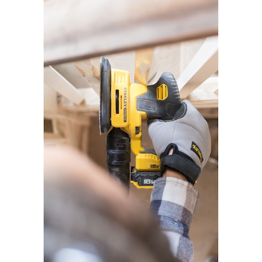 STANLEY FMCW210B cordless sander in use, yellow and black design, person wearing gloves sanding wood.