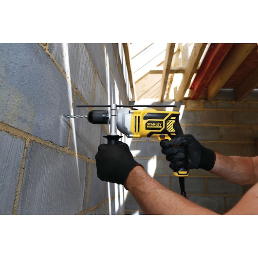 Photo of STANLEY FME140K hammer drill in use on a masonry wall, worker holds tool with black gloves.