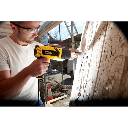 Photo of STANLEY FME670K heat gun used for paint removal on wood surface at construction site.