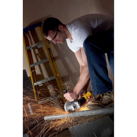 STANLEY FME821 angle grinder in use, cutting metal pipe, sparks flying, indoor workshop setting.