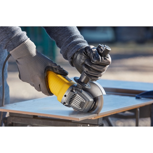 STANLEY FMEG210K angle grinder in use, yellow and black, cutting tile on workbench.
