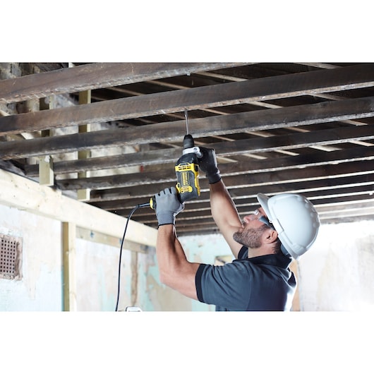 STANLEY FMEH750K corded drill used overhead on wooden beams, side angle, construction setting.