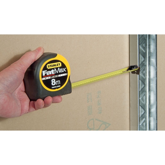 STANLEY FMHT0-33868 tape measure held in hand, yellow blade extended against drywall.