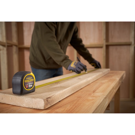 STANLEY FMHT0-33868 FATMAX tape measure on wooden beam in workshop, person marking measurements.