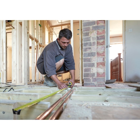 STANLEY FMHT0-36326 tape measure used by worker measuring copper pipes in home construction.