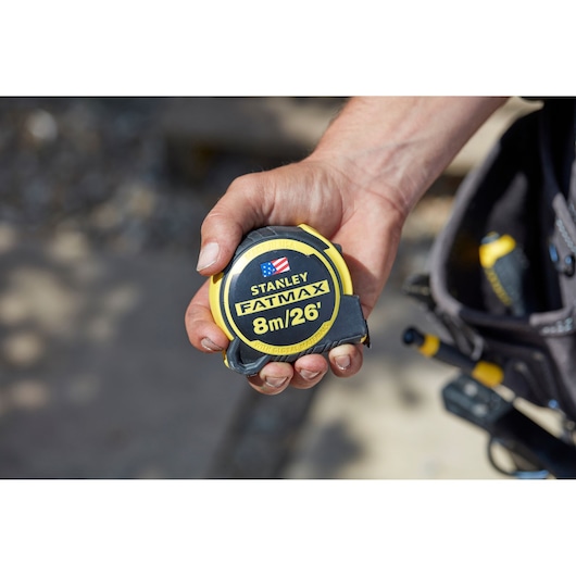STANLEY FMHT0-36326 FATMAX tape measure held in hand, black and yellow, 8m/26ft length, photography.