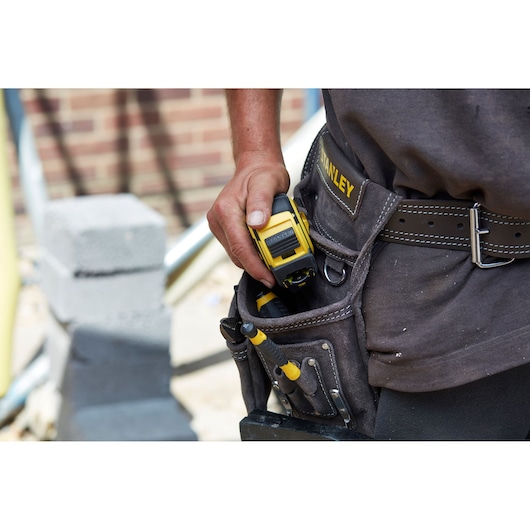Photo of STANLEY FMHT0-36326 tape measure in tool belt pouch at hip, with hand gripping yellow and black tool.
