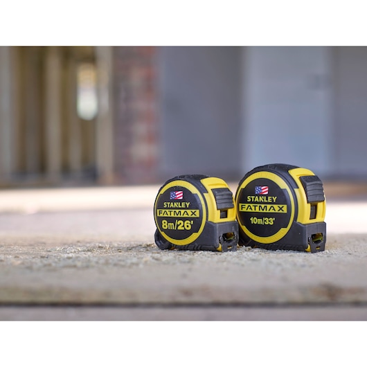 Photo of STANLEY FMHT0-36326 FATMAX tape measures, 8m/26' and 10m/33', black and yellow, on concrete surface.