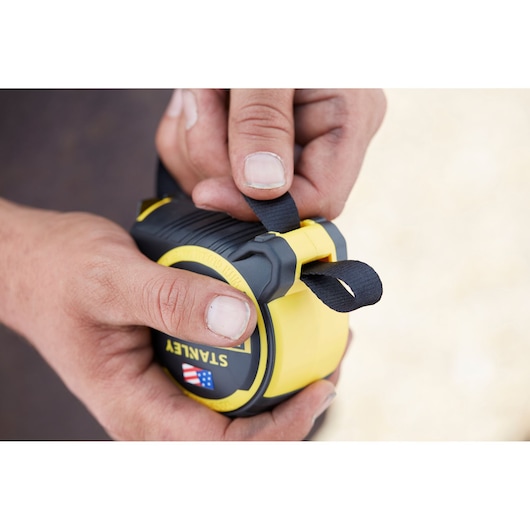 Photo of STANLEY FMHT0-36326 tape measure held by hand, showing black strap and yellow casing.