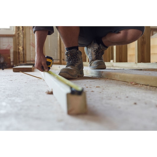 Photo of STANLEY FMHT0-36327 tape measure in use, measuring a wooden beam on a construction site floor.