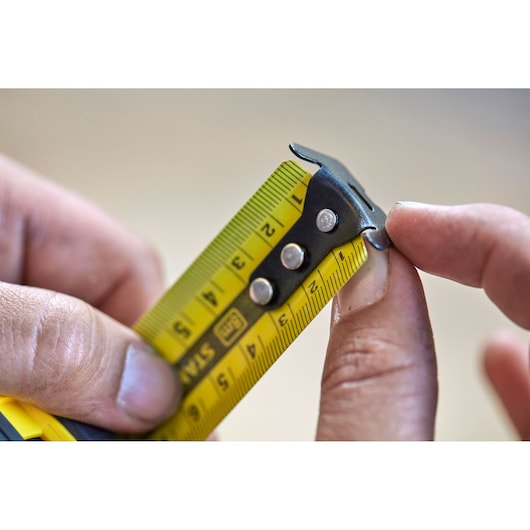 Photo of STANLEY FMHT0-36327 tape measure tip, yellow blade, black metal hook held between fingers.
