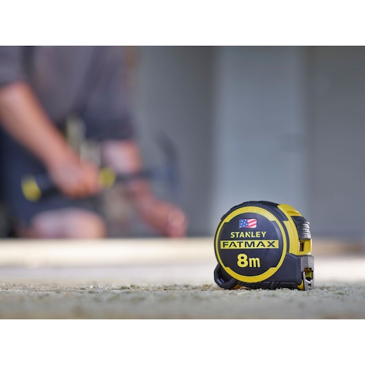 Photo of STANLEY FMHT0-36327 FATMAX 8m tape measure, black and yellow casing, on construction site floor.