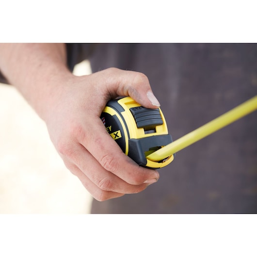 STANLEY FMHT0-36327 tape measure held in hand, yellow and black design, close-up view.