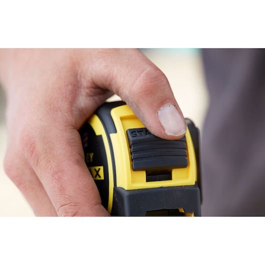 Stanley FMHT0-36327 tape measure close-up, black and yellow, thumb on lock slider.