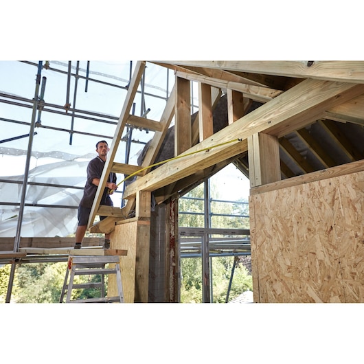 STANLEY FMHT0-36336 tape measure used for measuring wooden beams at a construction site, photography.