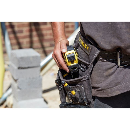 STANLEY FMHT0-36336 tape measure in a tool belt, close-up, construction site background.