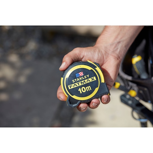 STANLEY FMHT0-36337 tape measure, FatMax 10m, yellow and black casing, held in a hand, product photography.