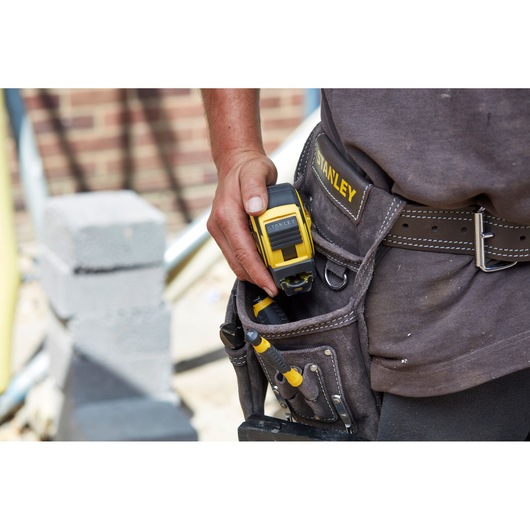 STANLEY FMHT0-36337 tape measure in a tool belt pocket with screwdrivers on a construction site.
