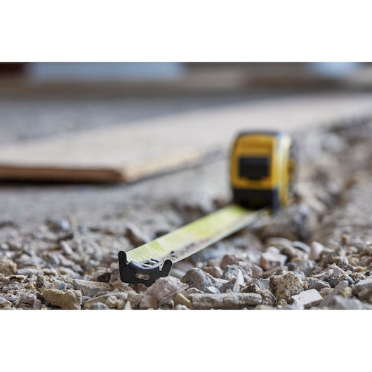 STANLEY FMHT0-36337 tape measure extended on rough gravel surface, close-up photography.