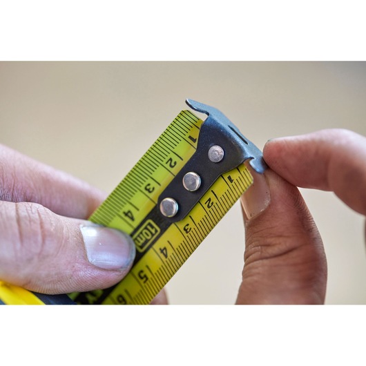 STANLEY FMHT0-36337 photography of yellow tape measure blade close-up held between fingers.