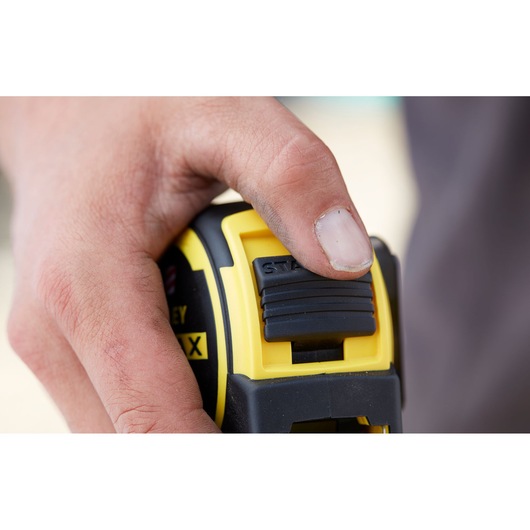 Photo of STANLEY FMHT0-36337 tape measure lock button in use, close-up on yellow and black body.