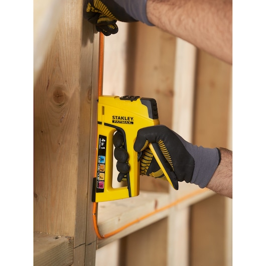 STANLEY FMHT0-70411 stapler tacker in use against wooden beam, yellow with black grip, FATMAX series.
