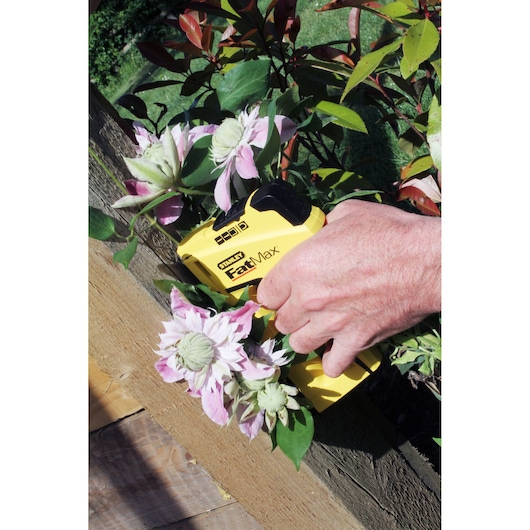 Photo of STANLEY FMHT0-70411 stapler in yellow, held by hand, fastening plants to wooden surface outdoors.