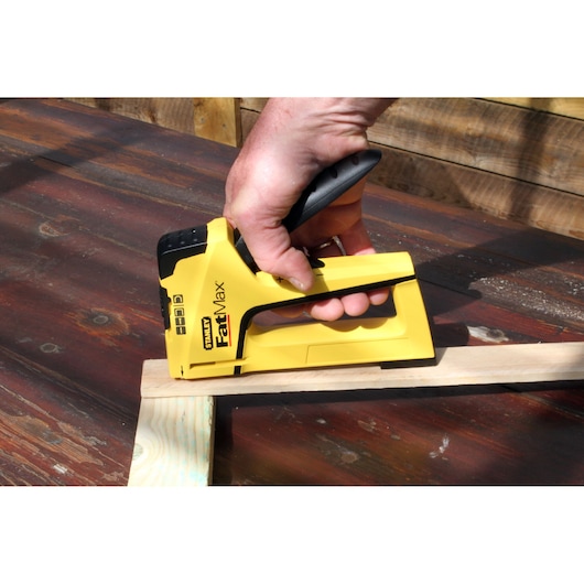 STANLEY FMHT0-70411 FatMax stapler in use, yellow and black, held on wooden boards outdoors.