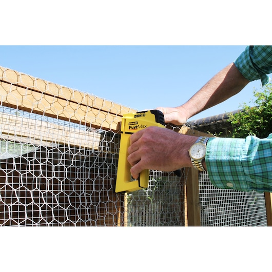 STANLEY FMHT0-70411 photography of yellow staple gun fastening wire mesh to wooden frame outdoors.