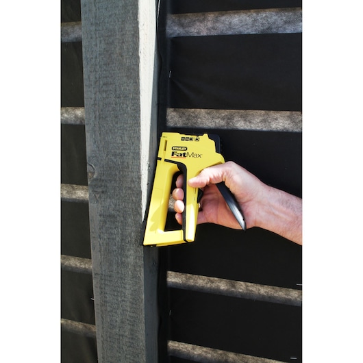 STANLEY FatMax FMHT0-70411 staple gun in use against a wooden beam, held by hand.