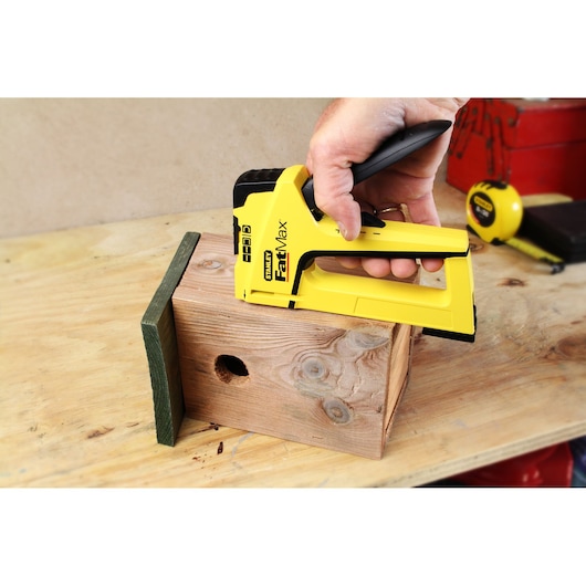 Photo of STANLEY FMHT0-70411 hand stapler fastening wood on a workbench.