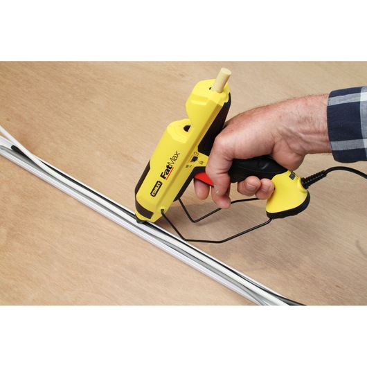 Photo of STANLEY FMHT0-70418 yellow FatMax glue gun applying adhesive to white strips on wood.