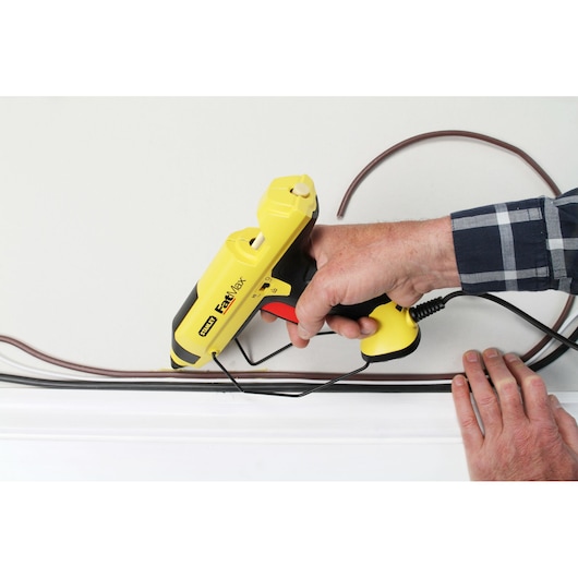 STANLEY FMHT0-70418 glue gun held against wall, applying adhesive to cables, close-up photo.