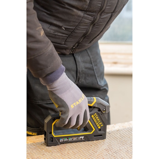 Photo of STANLEY FMHT0-80550 hand stapler in use, worker wearing gloves securing mesh to wood.