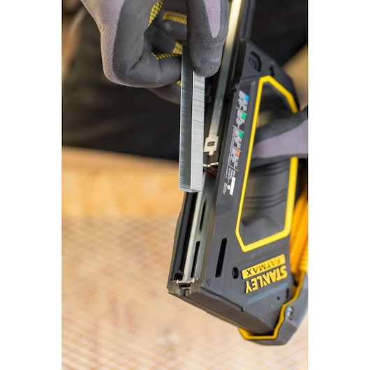 STANLEY FMHT0-80550 stapler being loaded with staples, close-up on gloved hand and open magazine.